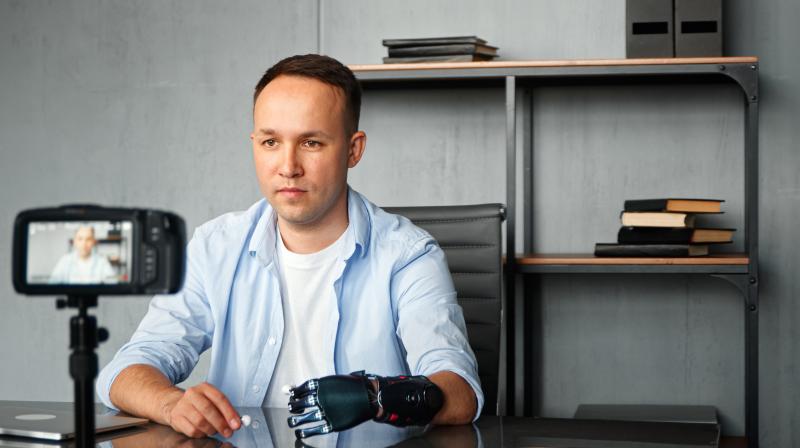 A cameraman with an upper limb prosthesis sitting at a desk filming