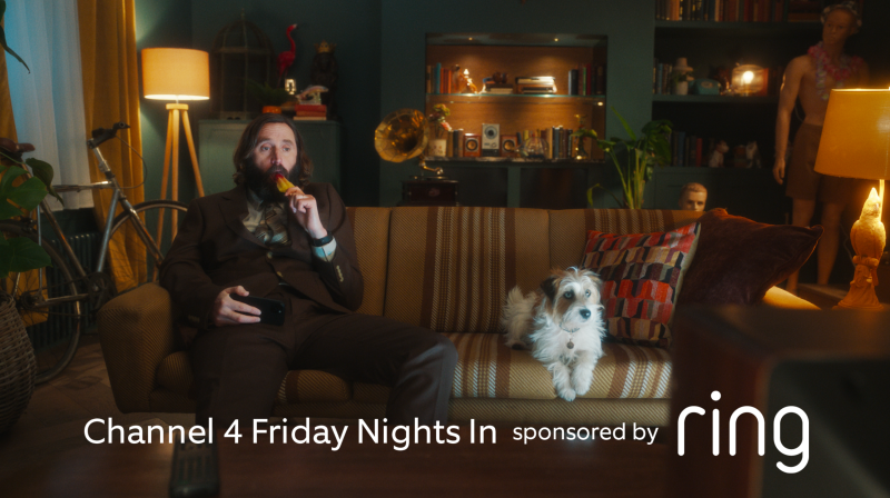 Joe Wilkinson eating an ice lolly on a sofa next to a Terrier 