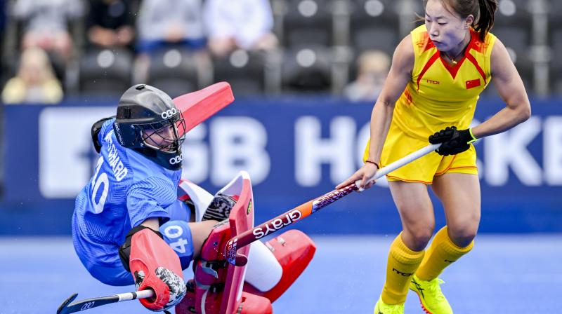 It shows two women hockey players. One is a goalie in a blue shirt diving to the right whilst a player for China dodges around them in the D. 