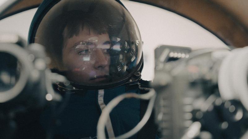 Close-up of Francis Bourgeois wearing a reflective space helmet and blue spacesuit, focused intently while operating equipment inside a spacecraft or simulation module.