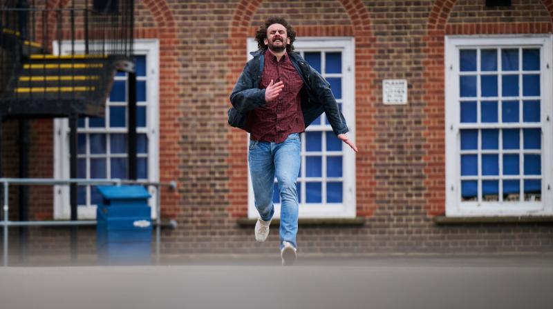 Brown haired man with beard wearing red shirt and jeans running