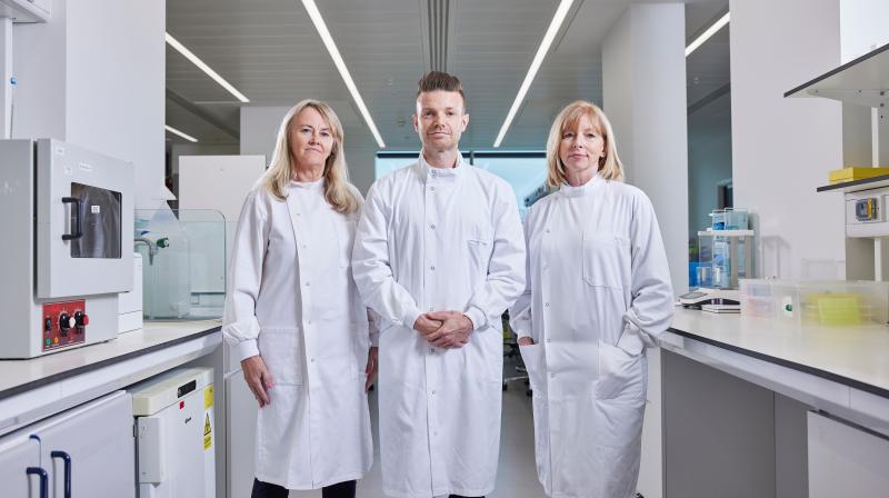 It shows three scientists standing together on the left is Professor Caroline Dive, then scientist Associate Professor Richard Mair and on the right is Professor Sarah Blagden.