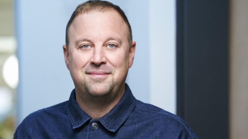 It shows a man looking directly at the camera, wearing a blue shirt