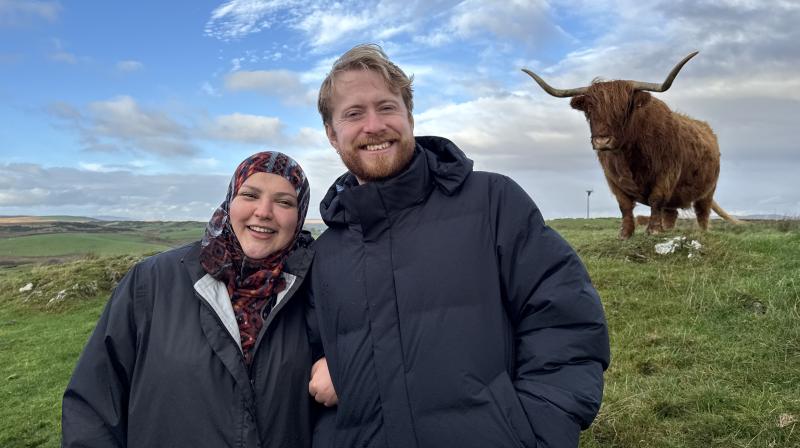 It shows two comedians Fatiha El-Ghorri and John Tothill smiling and in the background is a Highland Cow.