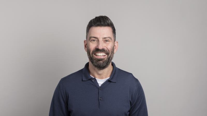 It shows Jonathan Allan in a navy shirt smiling at the camera. He is stood against a grey background.