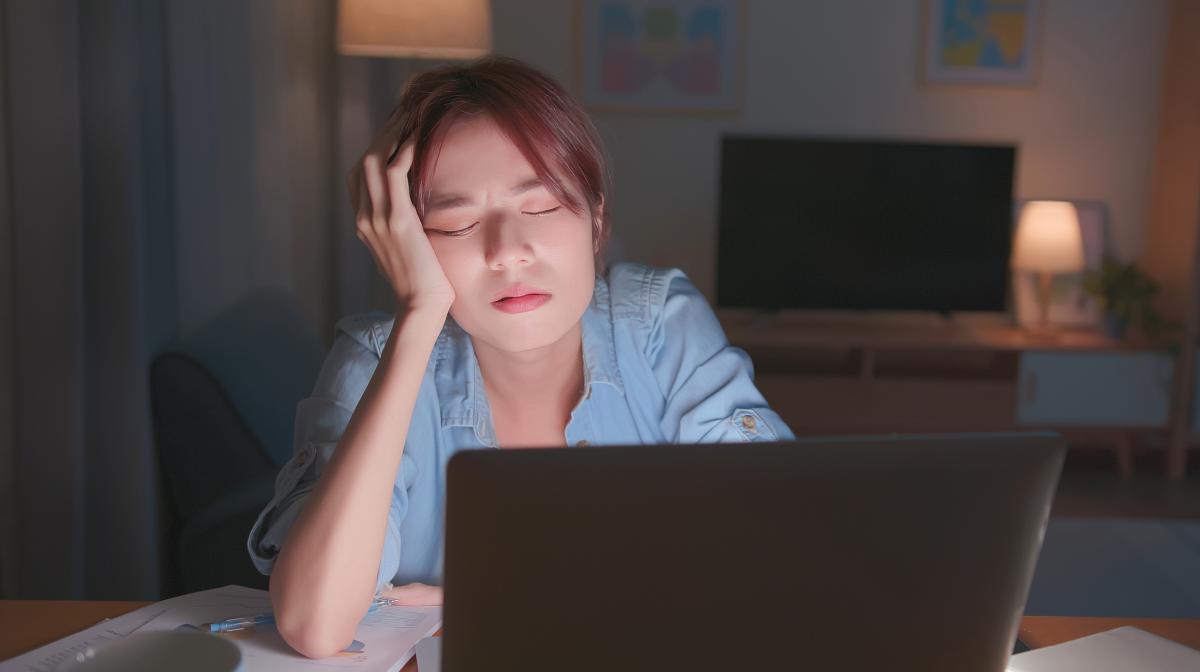 A woman with her head in her hand and eyes closed in front of a laptop