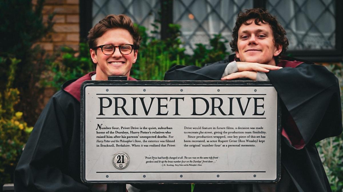 Max Fosh and Zac Alsop sitting on a bench behind a 'Privet Drive' sign from Harry Potter