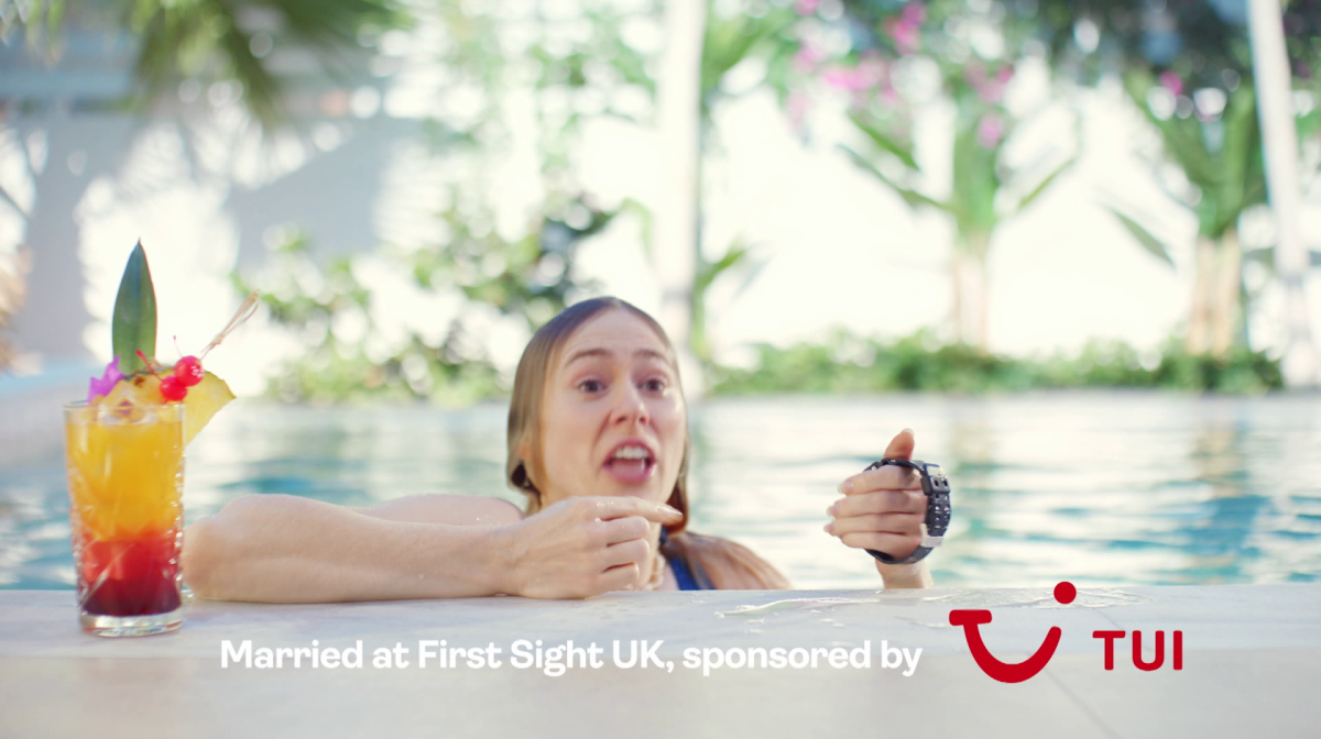 Image of a woman emerging from a swimming pool, timing how long she can breathe underwater with a watch in her hand.