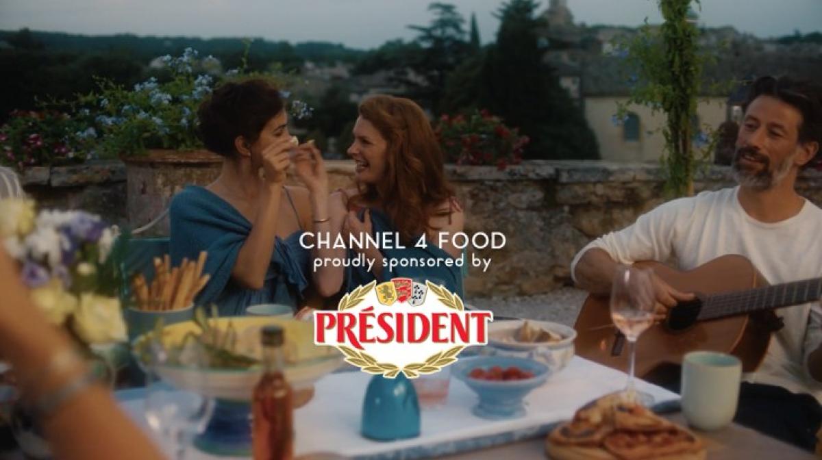 Two women enjoying dinner while a man plays the guitar, with the text 'Channel 4 Food, proudly sponsored by President'