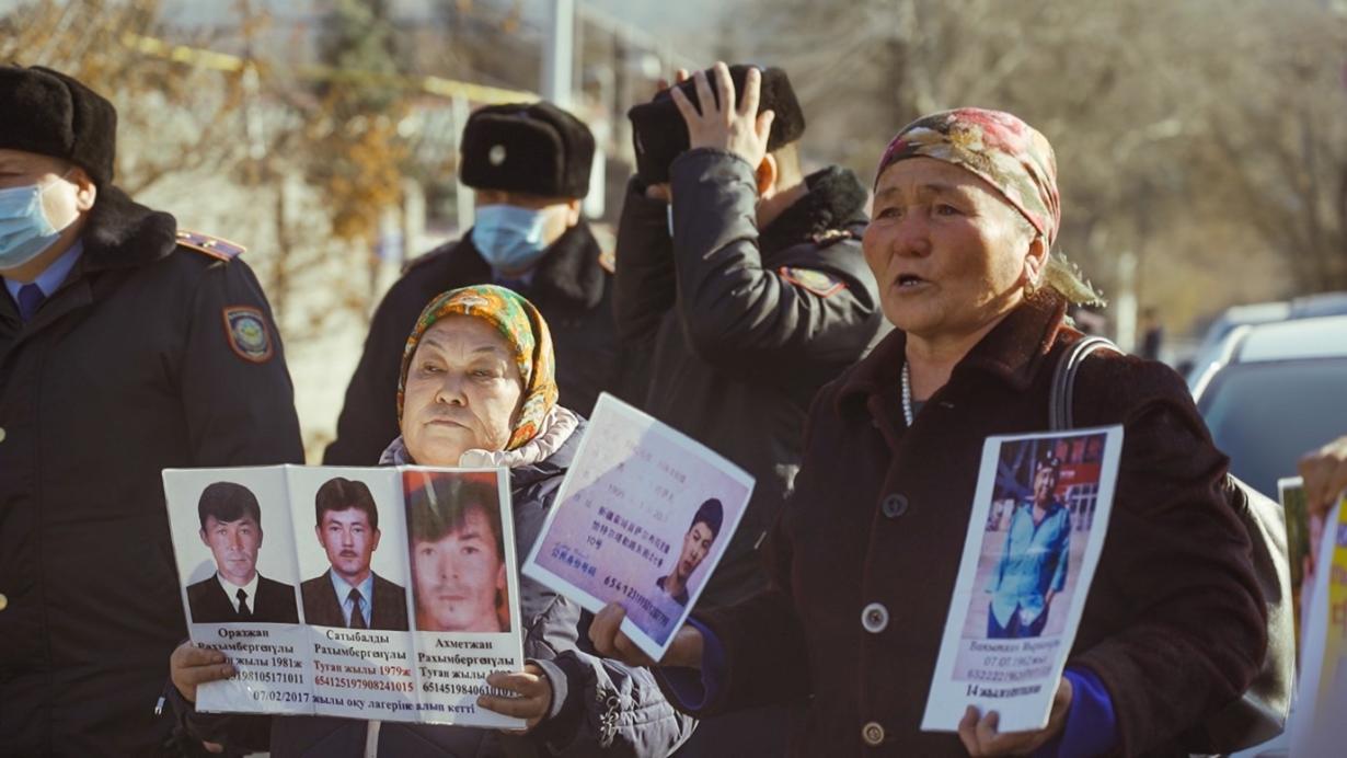 women holding up pictures of loved ones with soldiers in the background