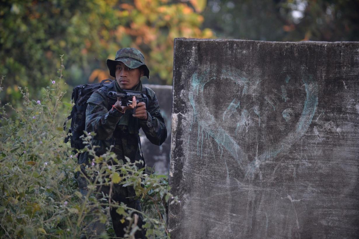soldier with gun in undergrowth next to heart graffiti on wall
