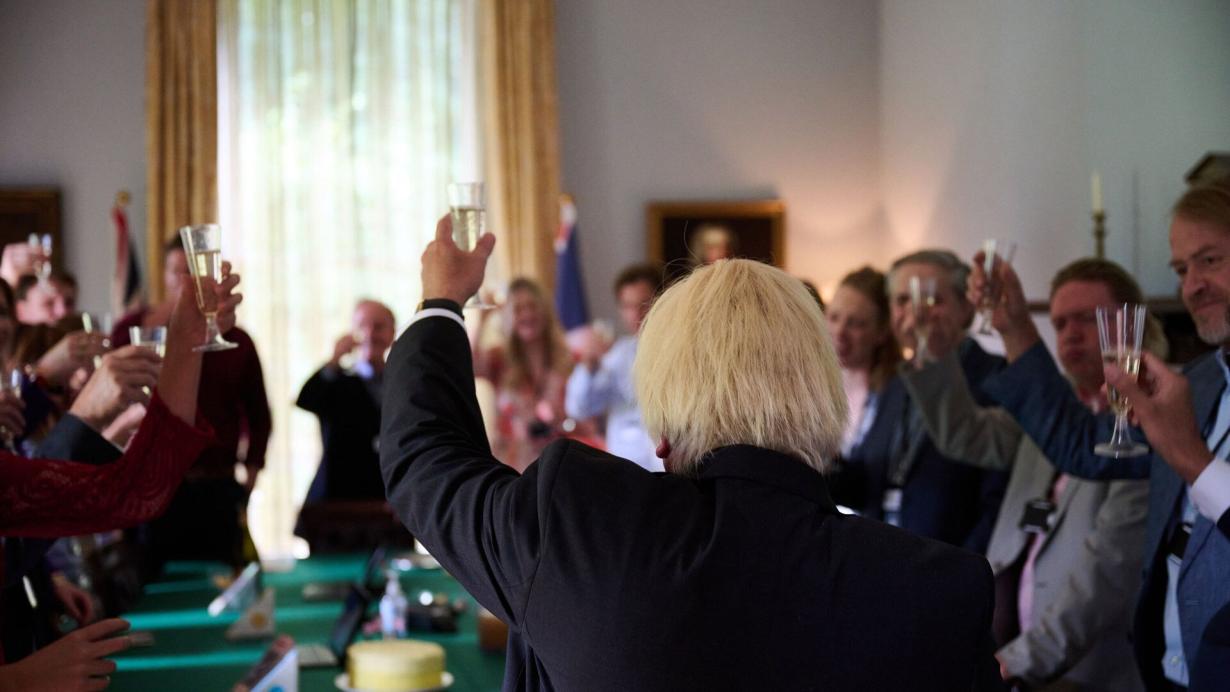 behind view of Boris Johnson facing party goers glasses raised