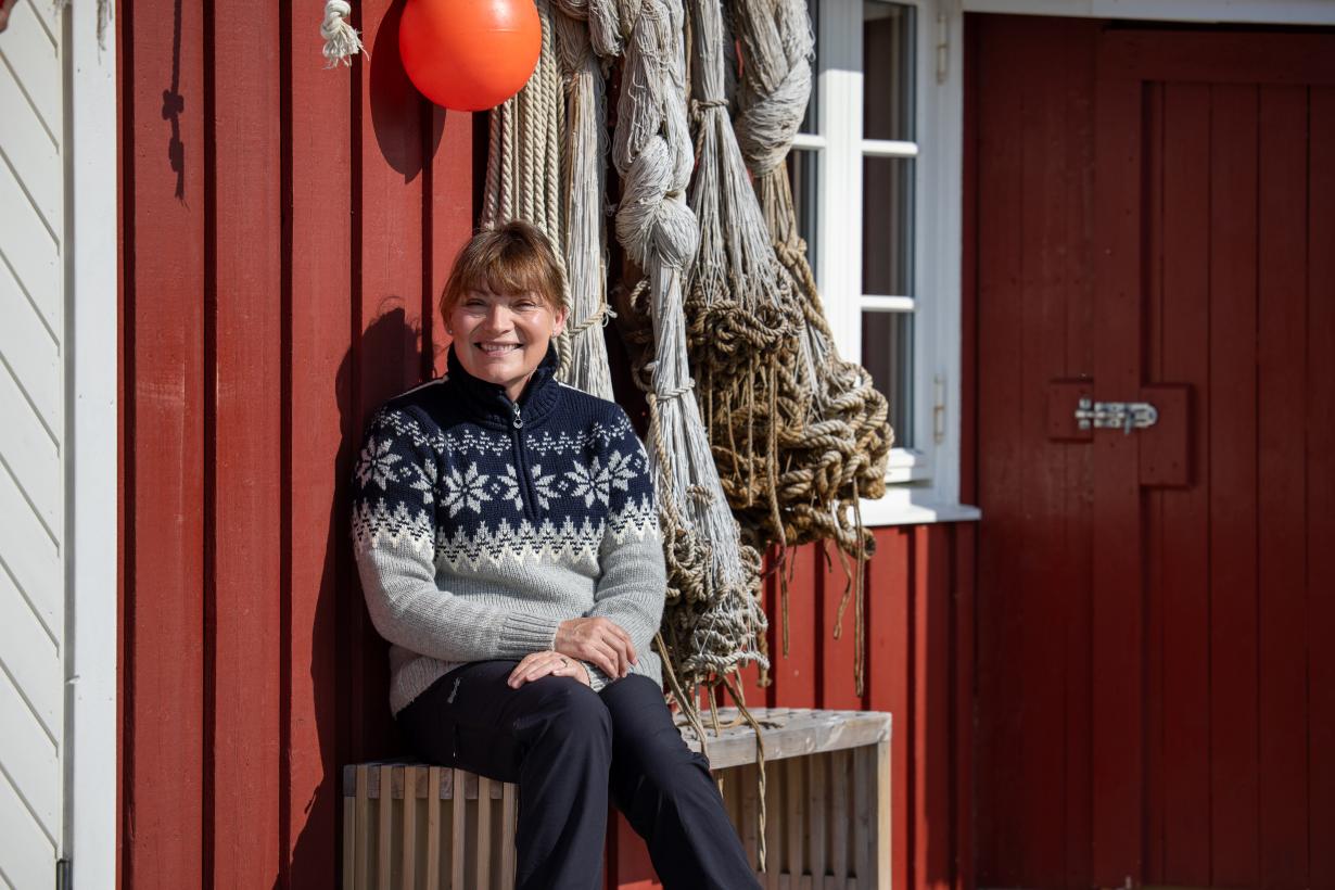 Lorraine Kelly sits by a red beach shack wearing a grey and blue fair isle jumper