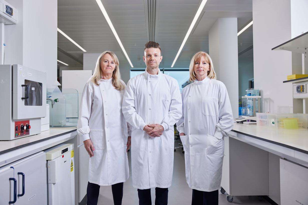 It shows three scientists standing together on the left is Professor Caroline Dive, then scientist Associate Professor Richard Mair and on the right is Professor Sarah Blagden.